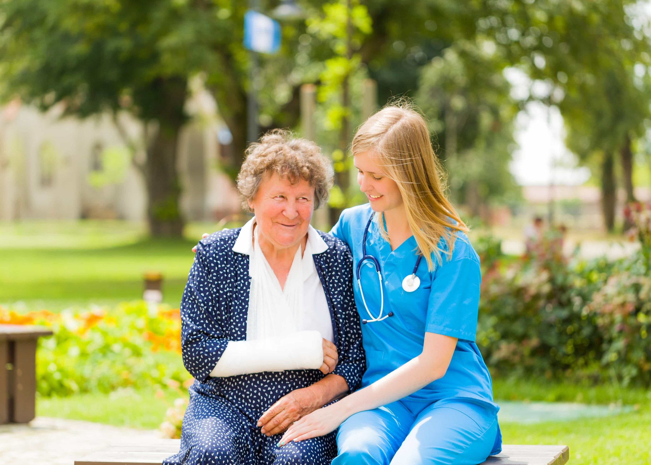 Comforting nurse with elderly woman patient who has plaster on her broken arm staying outdoors.