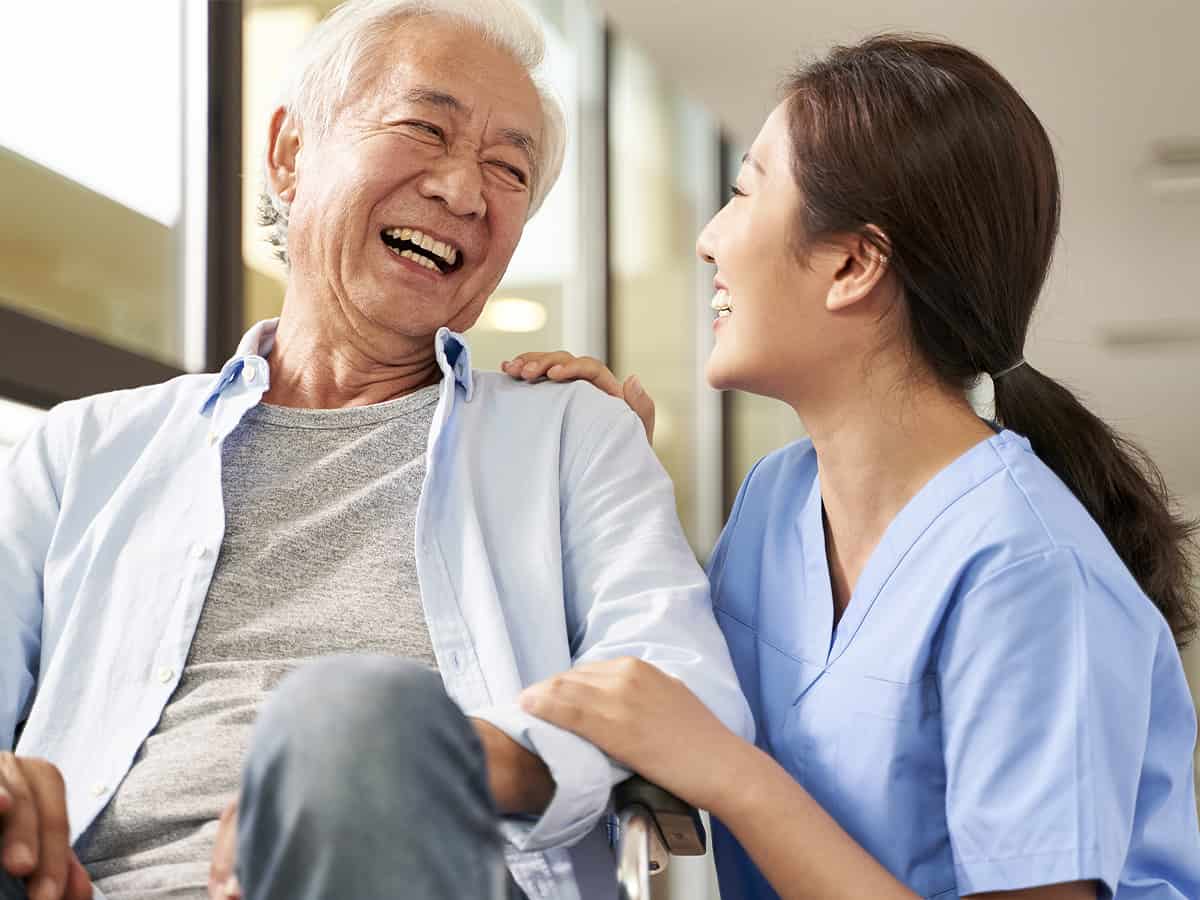 Elderly man and homecare nurse smiling and laughing
