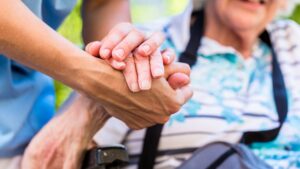 Caregiver holding the hand of elderly woman in wheelchair