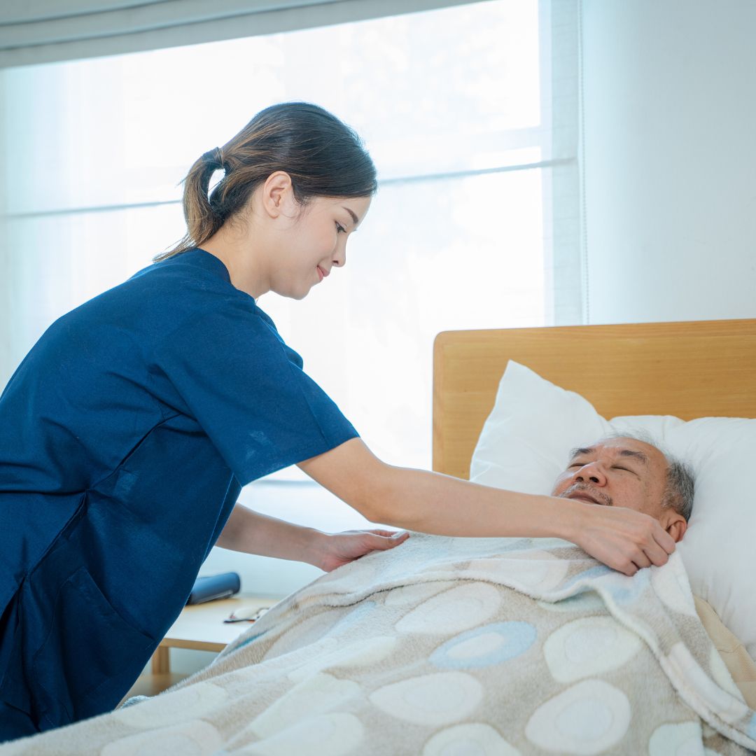 Nurse pulling quilt over elderly man